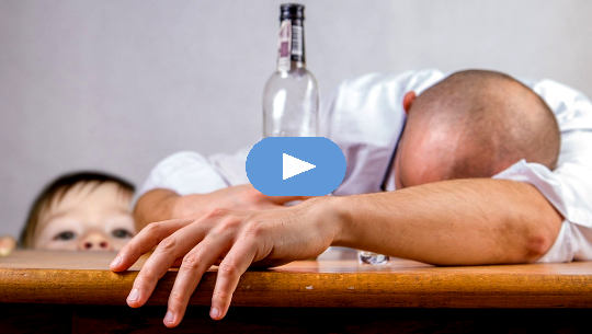 man passed out on a table with an empty bottle of alcohol with child looking on