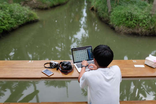 a young boy on a ship with his laptop open, and a camera and cell phone next to him.