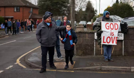 sports fanS on the way to a game, bystander holding a sign GOD IS LOVE