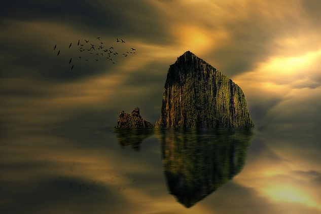 a big rock or boulder jutting out of the water and being reflected in the calm usrface of the lake