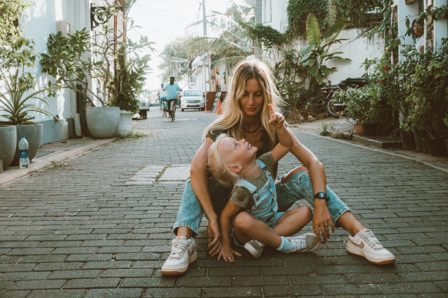 mother and child sitting on the ground in the middle of a cobblestone street