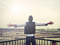 man standing looking out from a balcony with his arms wide open to the horizon