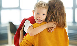 Child walking into school with backpack, smiling parent waving goodbye, representing a positive start to primary school.