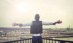 man standing looking out from a balcony with his arms wide open to the horizon