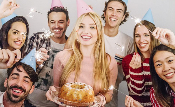 a group of friends smiling, one of them holding a birthday cake