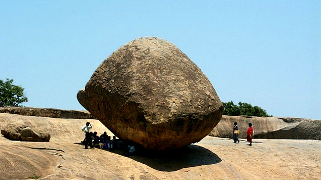 people sitting in the shade of a huge rock