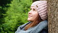 smiling woman resting against a tree trunk