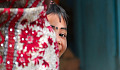 a young East-Indian girl, with a bindi dot or kala tikka on her forehead, and she is peeking out from behind something in a game of hide-and-seek