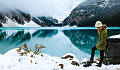 young woman standing in the snow next to a lake