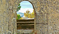 An open gate in a stone wall, opening up to a beautiful nature scene.