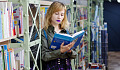 a young woman standing by a bookshelf reading a book