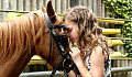 a young girl leaning her face on a horse's forehead