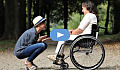 caring person squatting down in front of another in a wheelchair