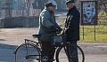 two older men speaking in the street, one is standing next to a bicycle