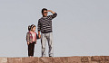 a father and daughter standing on a stone wall with the father looking into the distance