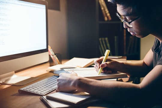 A young man sits in front of a computer screen highlighting notes