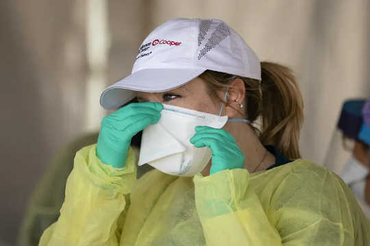 A woman pinching the nose of her mask to ensure a good fit.