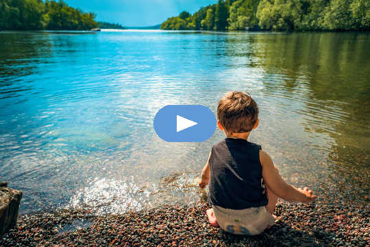 young child sitting at the edge of a peaceful lake