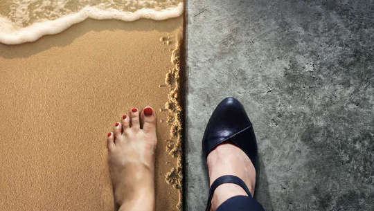 Split view of 2 feet: 1 barefoot on a beach, the other in black heels on a polished floor