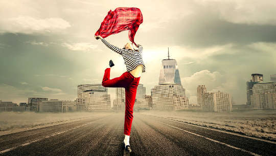 woman dancing in the middle of an empty highway with a city skyline in the background