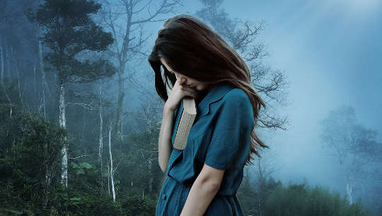 Woman, looking sad, holding a thick closed book and hanging her head 