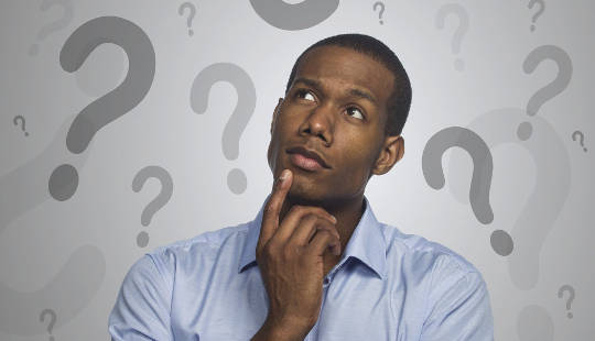 man with a finger on his chin looking up at a backdrop of question marks