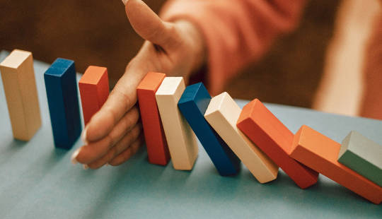 a hand stopping colorful dominos from falling