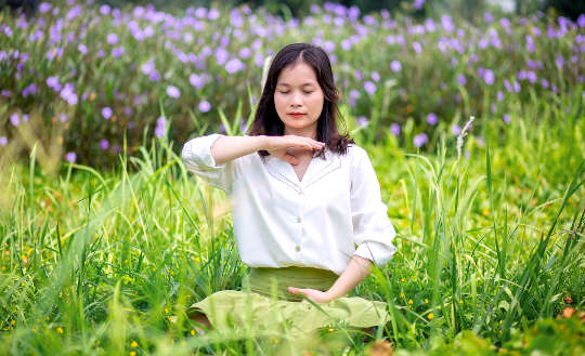 a woman sitting with eyes closed in a meadow