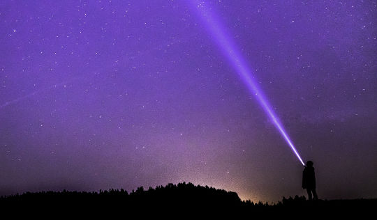 a child shining a flashlight up into the nighttime starry sky