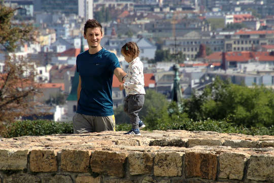 a young child walking on top of a stone wall with father standing by smiling and holding the child's hand