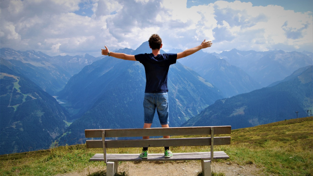 young man,with arms wide open, standing on a bench