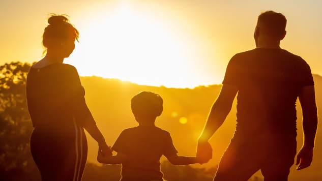 a couple holding hands of their child facing the setting sun