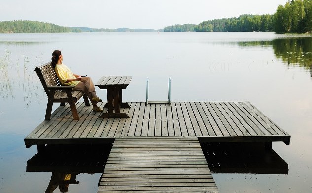 woman sitting on a bench on a platform dock surrounded by a very calm lake