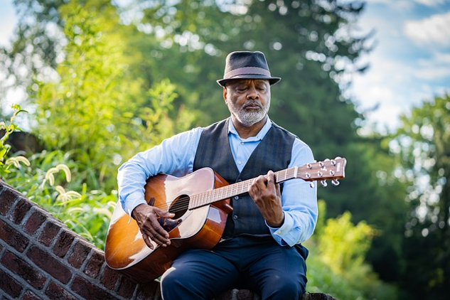 a man sitting on a brick fence and playing a guitar