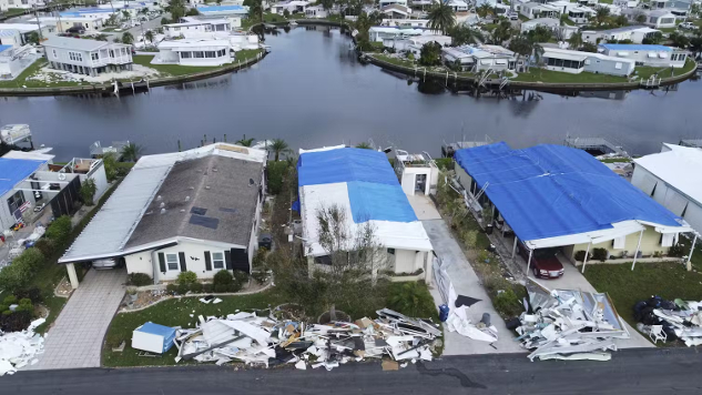 A flood-swollen canal is menacingly visible behind a row of hurricane-battered houses.