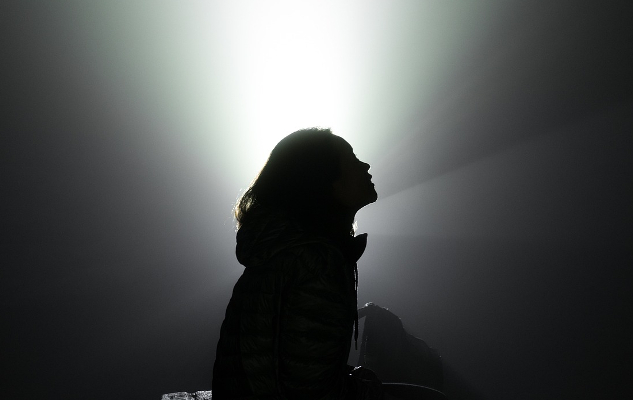 a woman in silhouette, sitting with a bright sky in the background