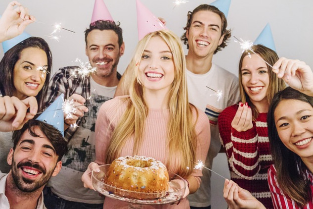 a group of friends smiling, one of them holding a birthday cake