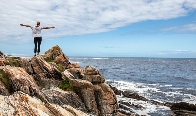 a person standing on rocks overlooking the ocean and the sky with arms wide open