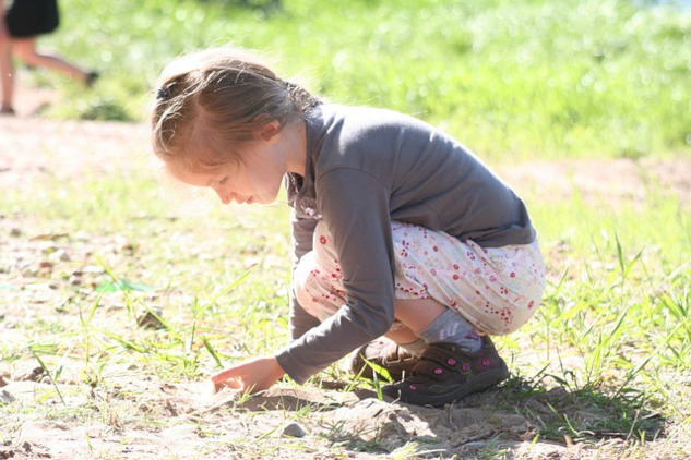 young girl squatting down to the earth and holding a plant