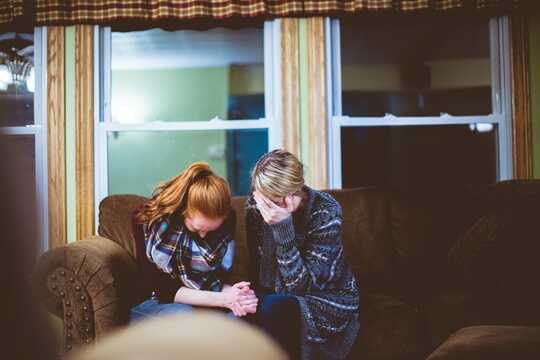 Two women sit on a couch, appear distressed.