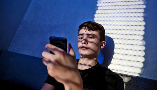 A teen boy sits up in bed reading his phone