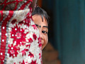 a young East-Indian girl, with a bindi dot or kala tikka on her forehead, and she is peeking out from behind something in a game of hide-and-seek