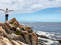 a person standing on rocks overlooking the ocean and the sky with arms wide open