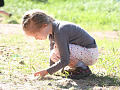 young girl squatting down to the earth and holding a plant