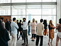 A diverse crowd of people in an office building, standing in small groups having conversations, representing networking in a professional environment.