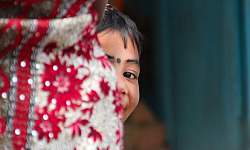 a young East-Indian girl, with a bindi dot or kala tikka on her forehead, and she is peeking out from behind something in a game of hide-and-seek