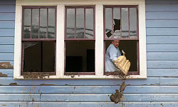 A powerful image showing flooded homes in a hurricane-impacted area, with people navigating through water-filled streets.