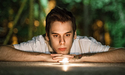 a young man laying down staring into a candle flame