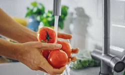 Fresh fruits and vegetables being washed under cold running water to remove dirt, bacteria, and pesticides.