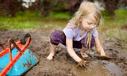 A joyful outdoor scene of children playing in a muddy garden area, hands covered in dirt, with smiles on their faces.